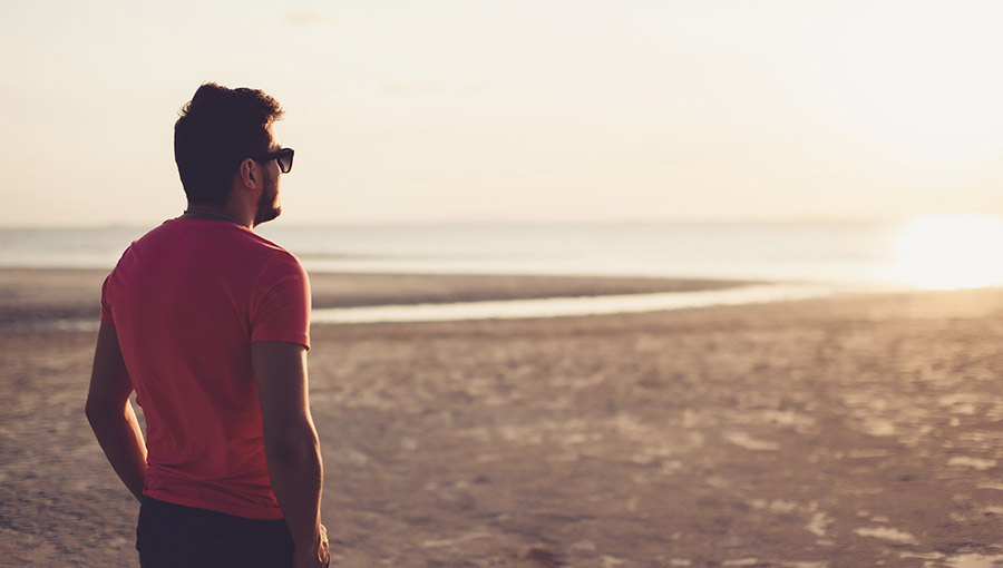 young man in sunglasses meets the sunset on the beach near the sea